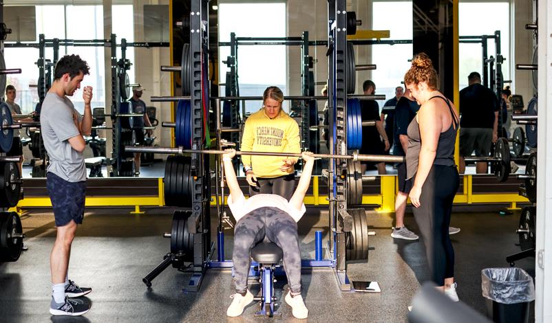 woman lifting bellbars with three coaches